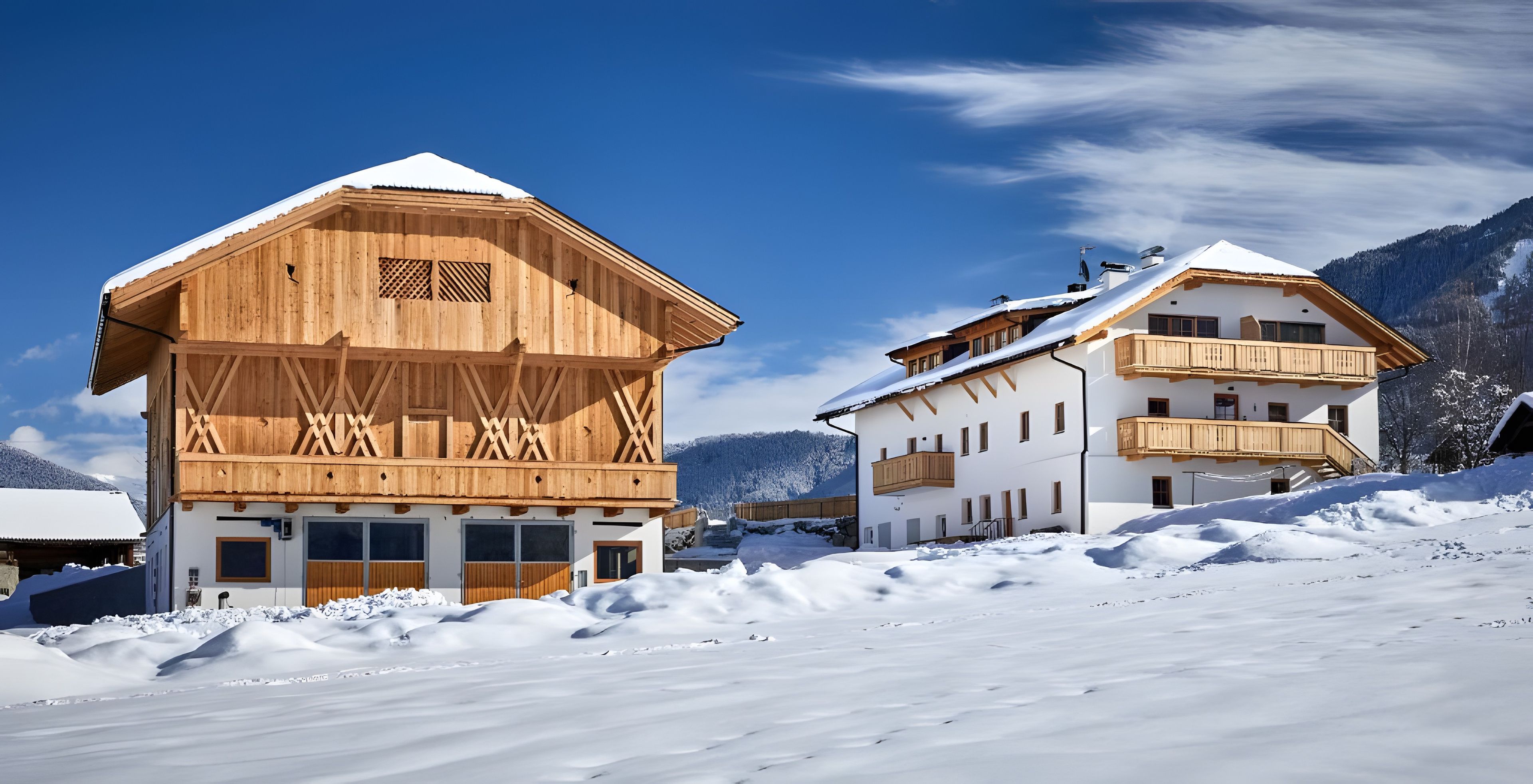 Zwei Holzhäuser mit Balkonen, umgeben von schneebedeckten Bergen.