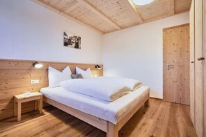 A bedroom with a wooden bed, bedside tables, a wall-mounted lamp, and a door. - Apartment 'Huberhof - Puschtra' (Santo Stefano)