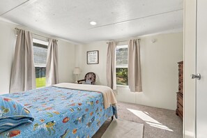 A bedroom with a bed, a nightstand, a lamp, a dresser, and a window with curtains. - A Cozy Place - Country/Beach Living (Beaufort)