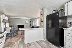 Une cuisine compacte avec un réfrigérateur noir, des meubles blancs et un petit îlot central.