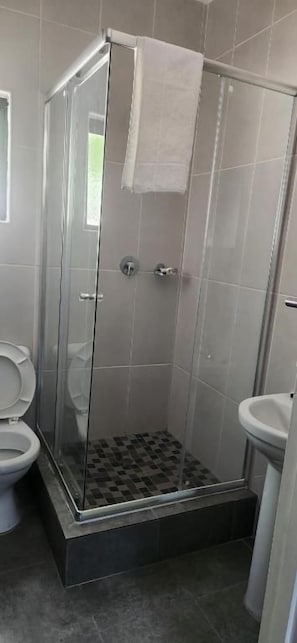 A shower enclosure with a glass door, a toilet, and a sink. - The Hornbill Lodge (Nata)