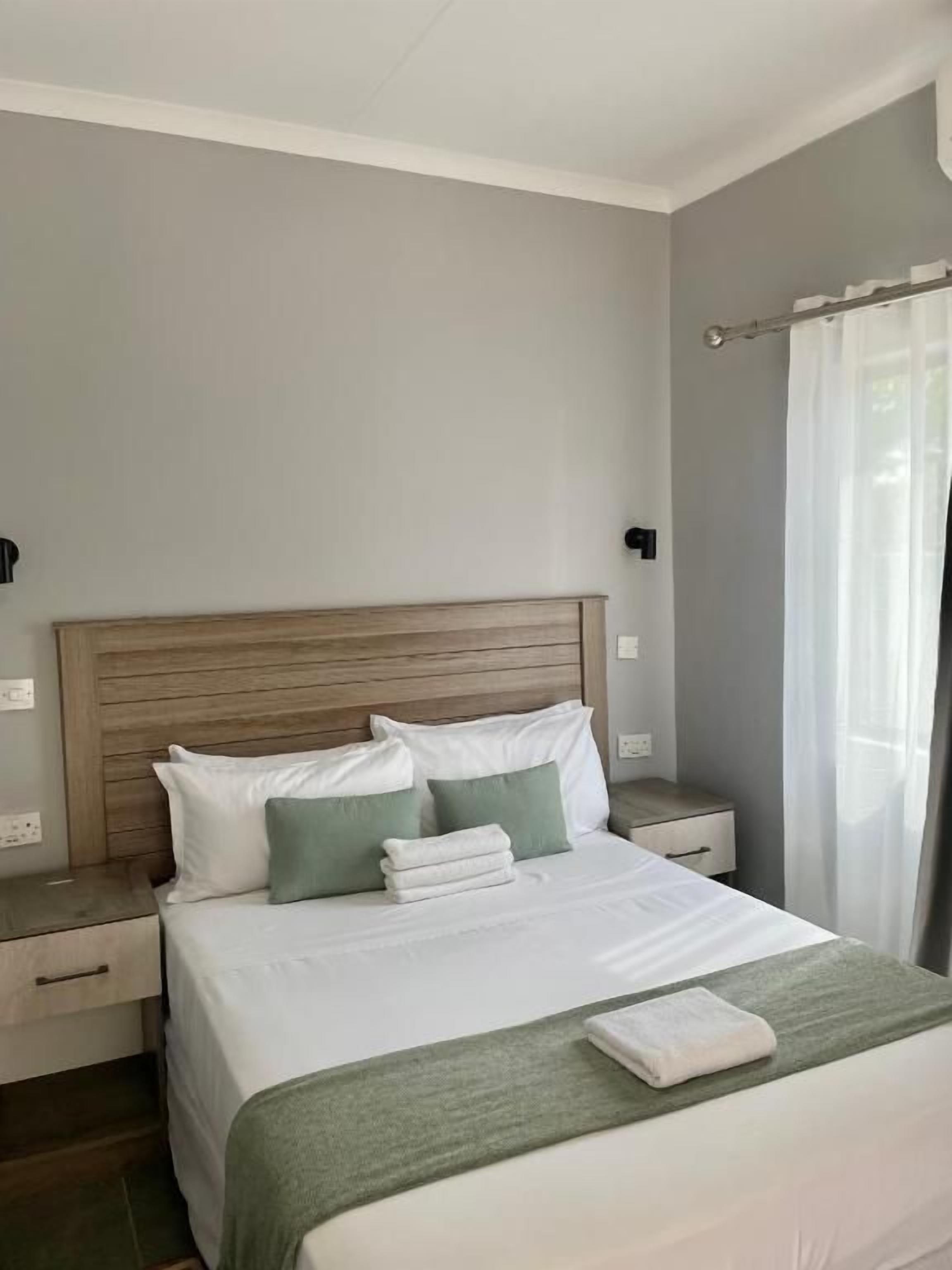 Una habitación de hotel con una cama, mesitas de noche, un cabecero de madera y una ventana con cortinas.