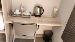 Ein kompaktes Hotelzimmer mit Küchenzeile, darunter eine Kaffeemaschine, ein Wasserkocher und ein Tablett mit Tassen und einer Flasche.