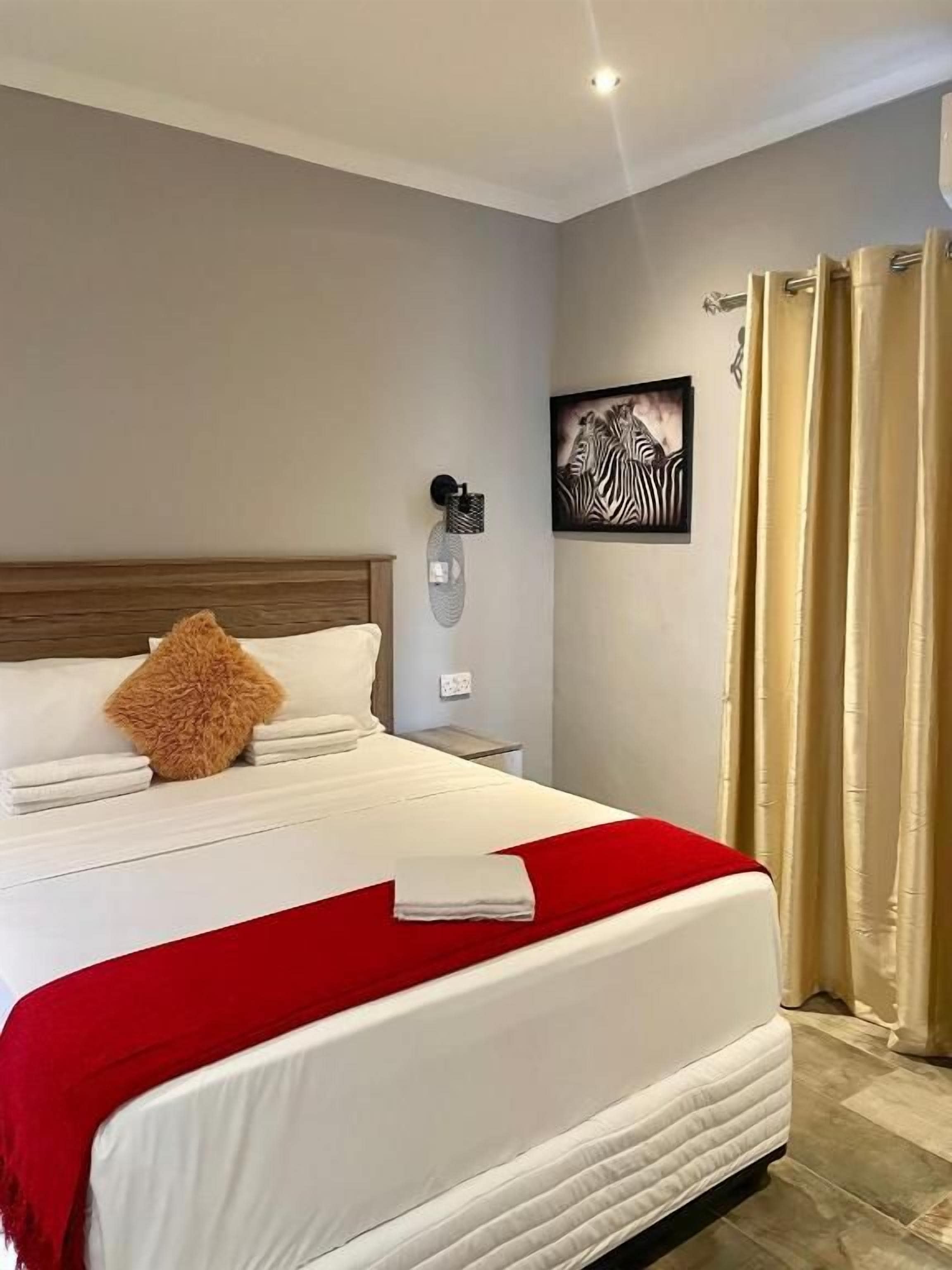A hotel room with a bed, a nightstand, a wall-mounted lamp, a framed artwork, and a curtain.