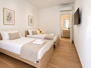 A hotel room with two beds, a TV mounted on the wall, and an air conditioning unit.