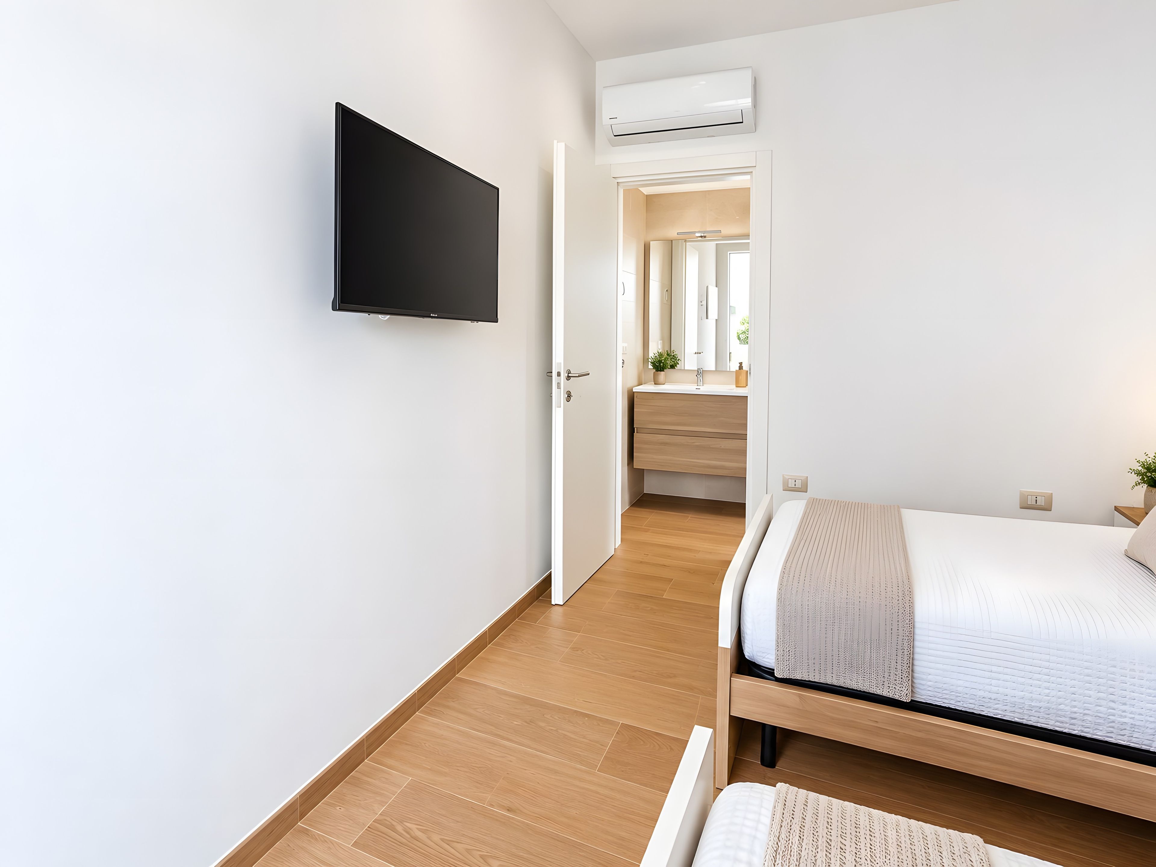Ein modernes Schlafzimmer mit einem flachbildfernseher an der Wand, einem hölzernen Bett mit weißer Matratze und Holzboden.