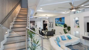 Un intérieur moderne comprenant un escalier, un coin repas et un salon doté d’un ventilateur de plafond.