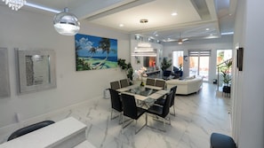 A modern dining area with a glass table and chairs, a painting of a tropical scene, and a ceiling fan. - Pool Townhome 250 Steps to Beach (South Padre Island)