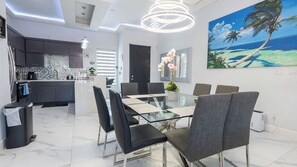 A modern dining area with a glass table, black chairs, and a painting of a beach scene. - Sleeps 12, Pool, Walk to Beach (South Padre Island)