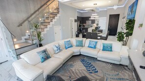 A modern living room with a white sectional sofa, a staircase, and a kitchen area. - Sleeps 12, Pool, Walk to Beach (South Padre Island)