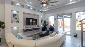 A modern living room with a large white sofa, a flat-screen TV, and a ceiling fan. - Sleeps 12, Pool, Walk to Beach (South Padre Island)