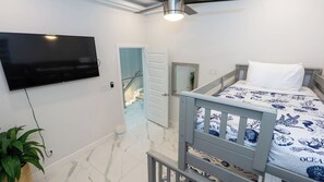 Ein Schlafzimmer mit Bett, einem an der Wand befestigten Fernseher, einer Tür zu einer Treppe und einer Zimmerpflanze.