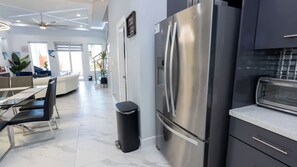 A modern kitchen with a stainless steel refrigerator, a built-in oven, and a dining area with a glass table and chairs. - Sleeps 12, Pool, Walk to Beach (South Padre Island)