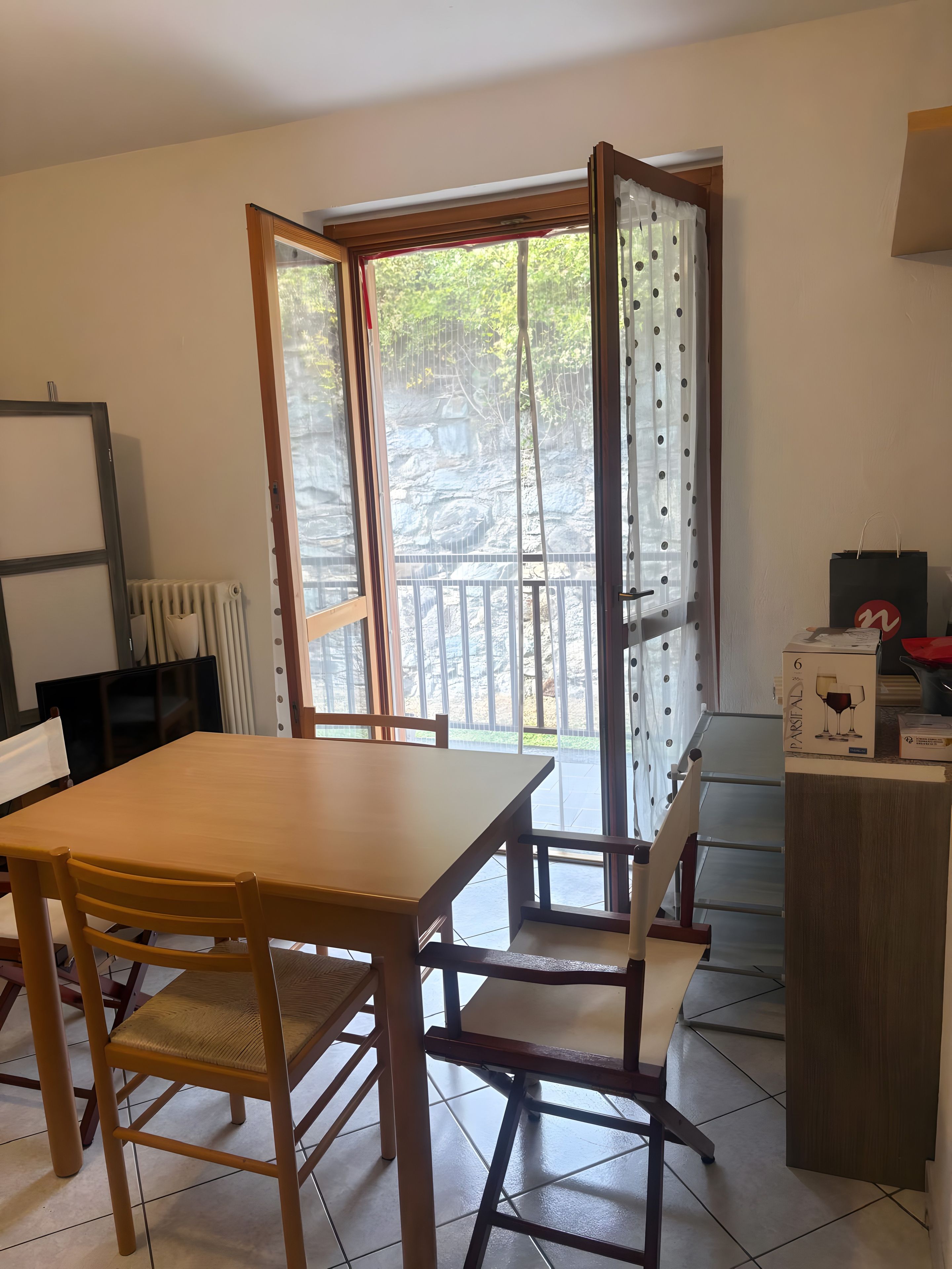 Une pièce avec une table et des chaises en bois, un radiateur, une fenêtre avec des rideaux et une boîte posée sur la table.