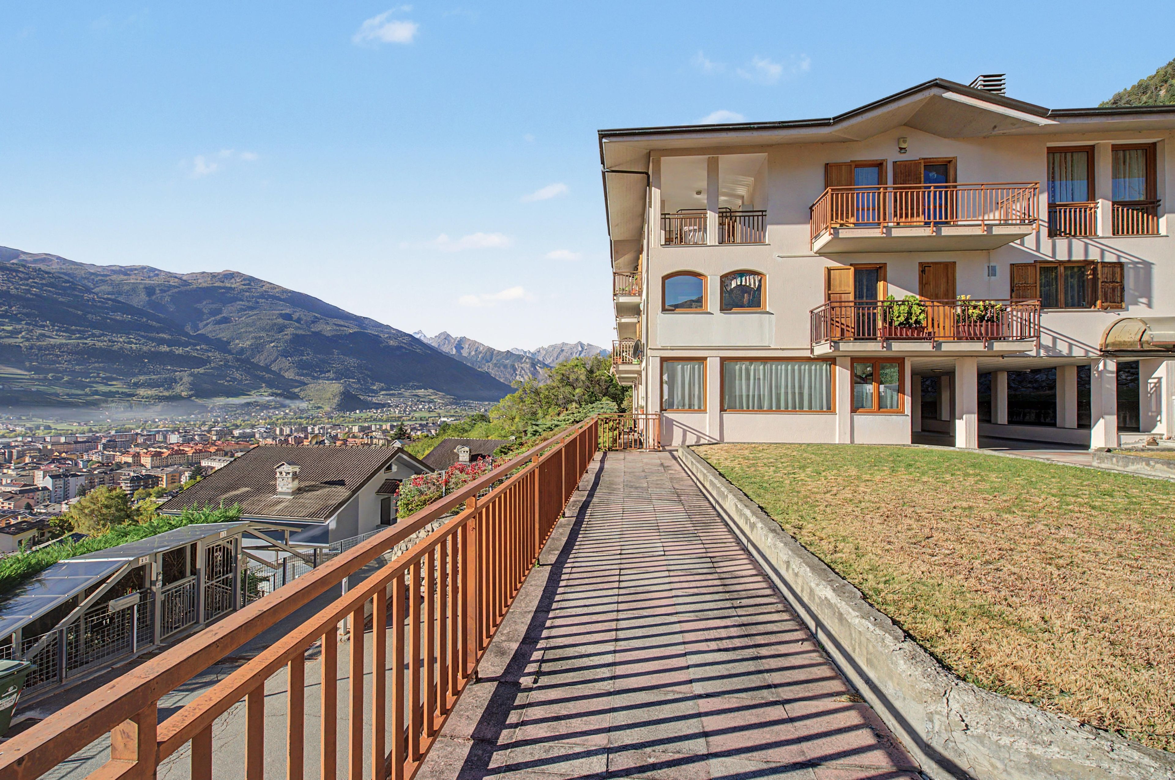 Un hôtel à plusieurs étages doté de balcons, d’une promenade dallée et offrant une vue sur un paysage montagneux.