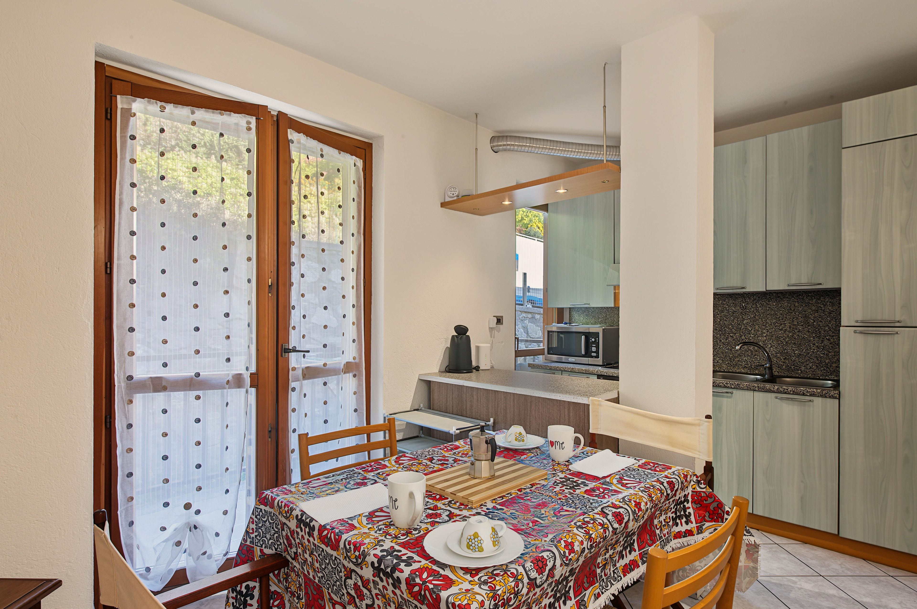 Un coin repas avec une table dressée pour deux personnes, une cuisine équipée d’appareils modernes et une vue par la fenêtre.