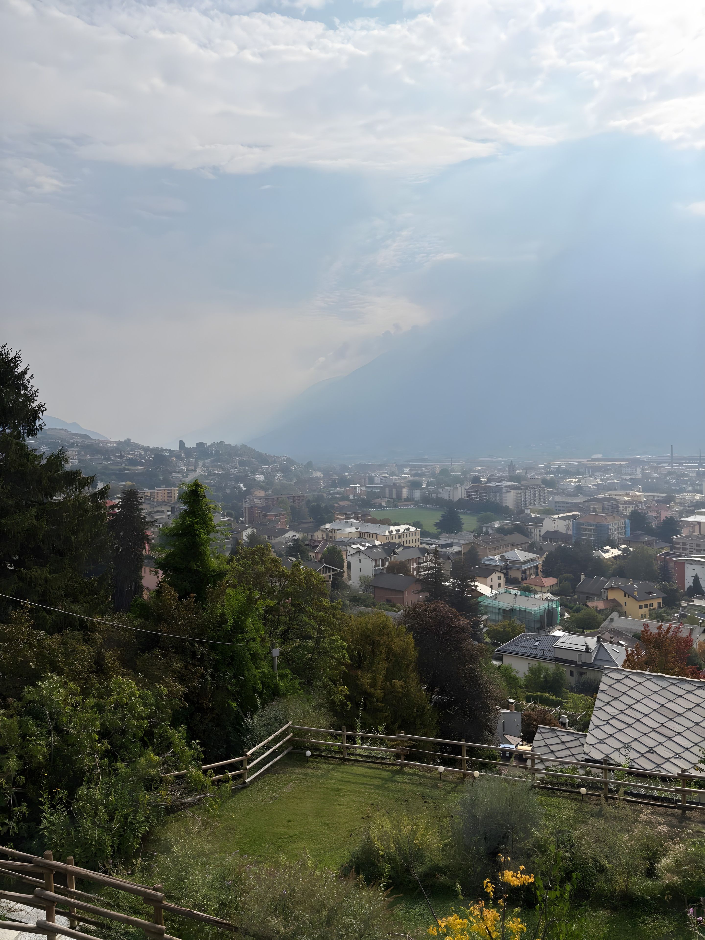 Un quartier résidentiel offrant une vue sur une ville lointaine, entouré de verdure et délimité par une clôture en bois.