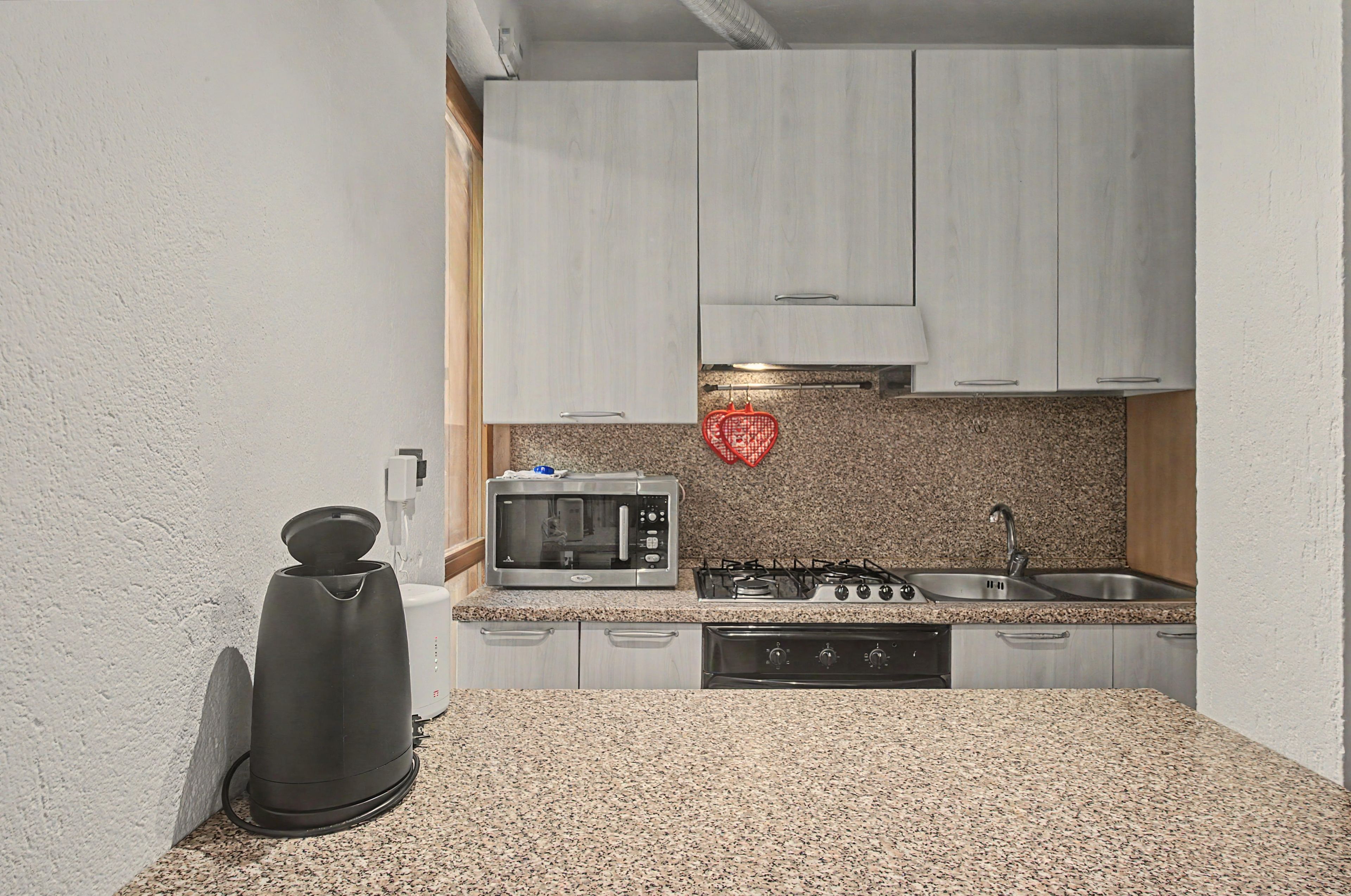 Una cocina compacta con gabinetes blancos, un microondas, una estufa y un lavabo.