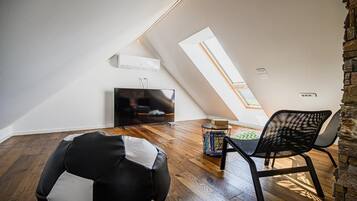 A modern loft bedroom with a sloped ceiling, a skylight, a flat-screen TV, a black and white bean bag, and a black mesh chair.