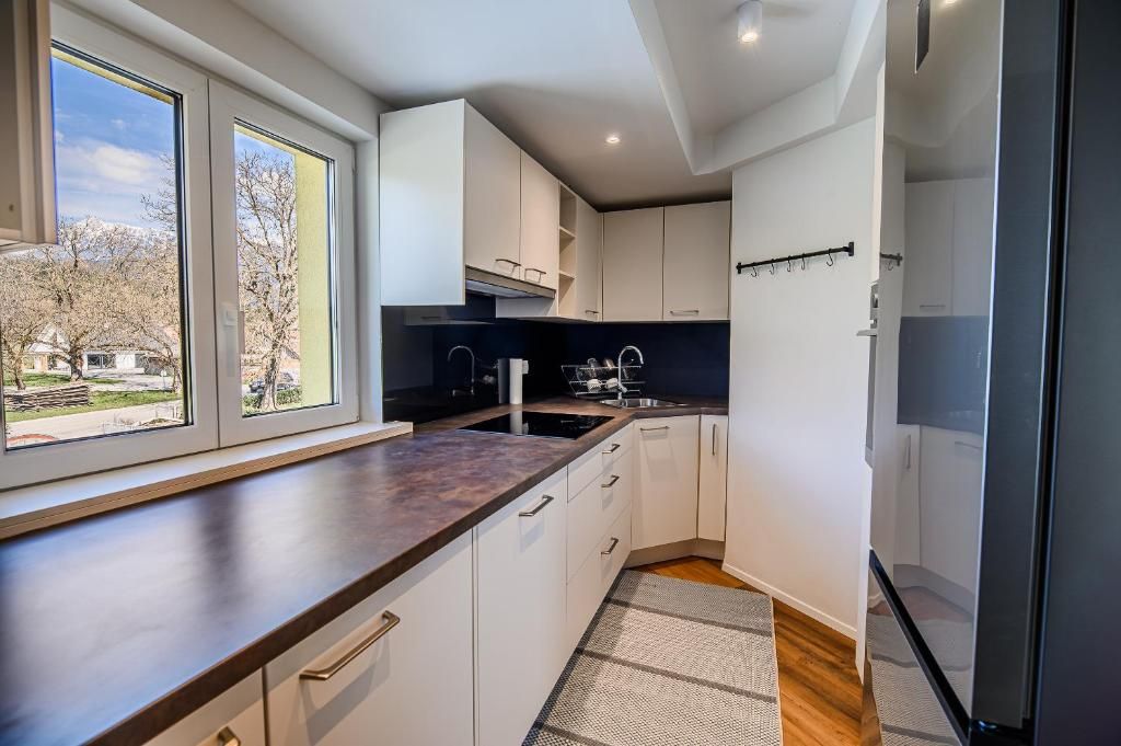 Cocina moderna con armarios blancos, encimera oscura y ventana con vistas a una zona residencial.