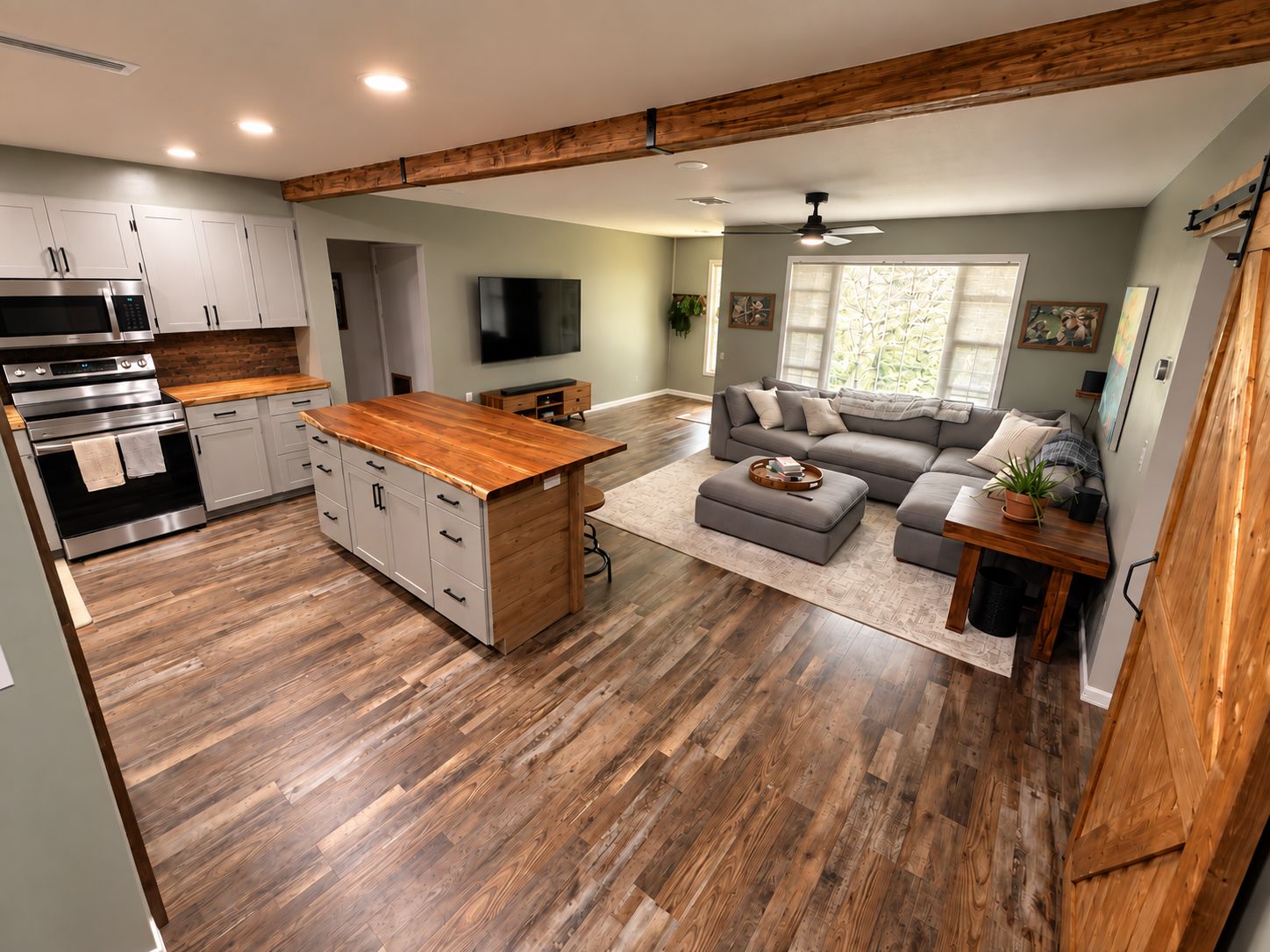 A modern kitchen with a central island, a dining area with a sofa, and a large window providing natural light.