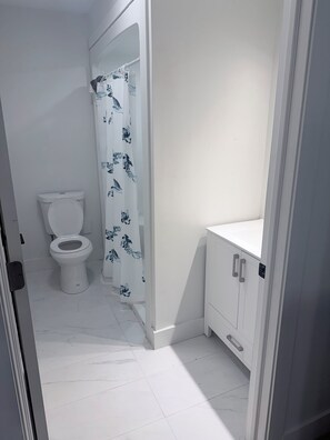 Ein Badezimmer mit Toilette, einer Duschkabine mit floralem Muster und einem weißen Schrank.