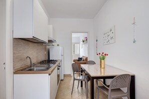 Une cuisine moderne dotée d’une cuisinière et d’un évier intégrés, un coin repas avec une table et des chaises, et un couloir menant à l’espace de vie.