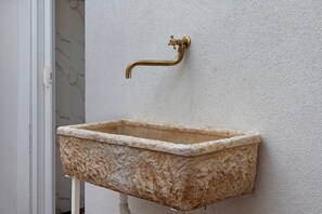 A rectangular stone sink mounted on a textured wall with a brass faucet. - Holiday Home 'Blue Wave' (Porto Cesareo)
