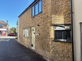 Un edificio de piedra con una puerta verde, un letrero que dice 'Baker Street Cottage' y un coche rojo estacionado.