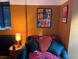 Una habitación con un sofá, una lámpara, un cartel enmarco y una planta en maceta.