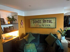 Una sala de estar con un sofá verde, una mesita con libros, un cartel en la pared y un radiador.