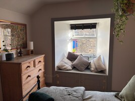 Un dormitorio con asiento empotrado junto a la ventana, cómoda de madera y cama con manta verde.