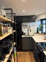 Una cocina moderna con un refrigerador negro, estantes de madera y un lavamanos.