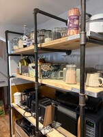 Una cocina con estantes que contienen frascos, botellas y una cafetera.