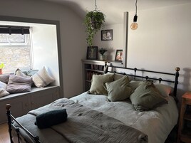 Un dormitorio con cama, ventana, estantería y plantas colgantes.