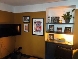 Una sala de estar con televisor de pantalla plana, obras de arte enmarcadas, un estante con adornos y una planta en maceta.