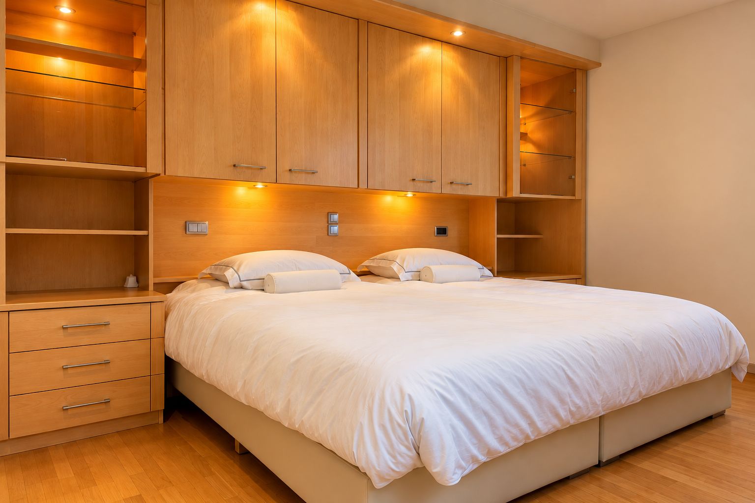 A bedroom with a large bed, wooden wardrobe, and built-in shelving.