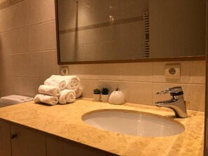 Ein Badezimmer mit Waschbecken, Spiegel, gestapelten Handtüchern und kleinen Topfpflanzen.