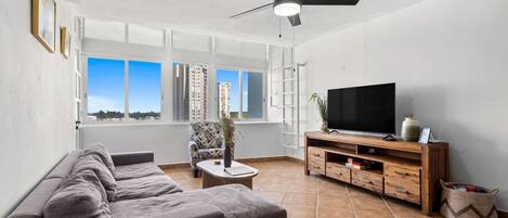 A living room with a sofa, TV, wooden entertainment unit, and a ceiling fan.