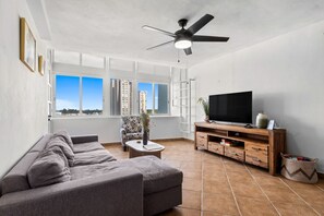 A living room with a sofa, TV, wooden entertainment unit, and a ceiling fan. - Oceanview Penthouse | Huge Private Terrace (Luquillo)