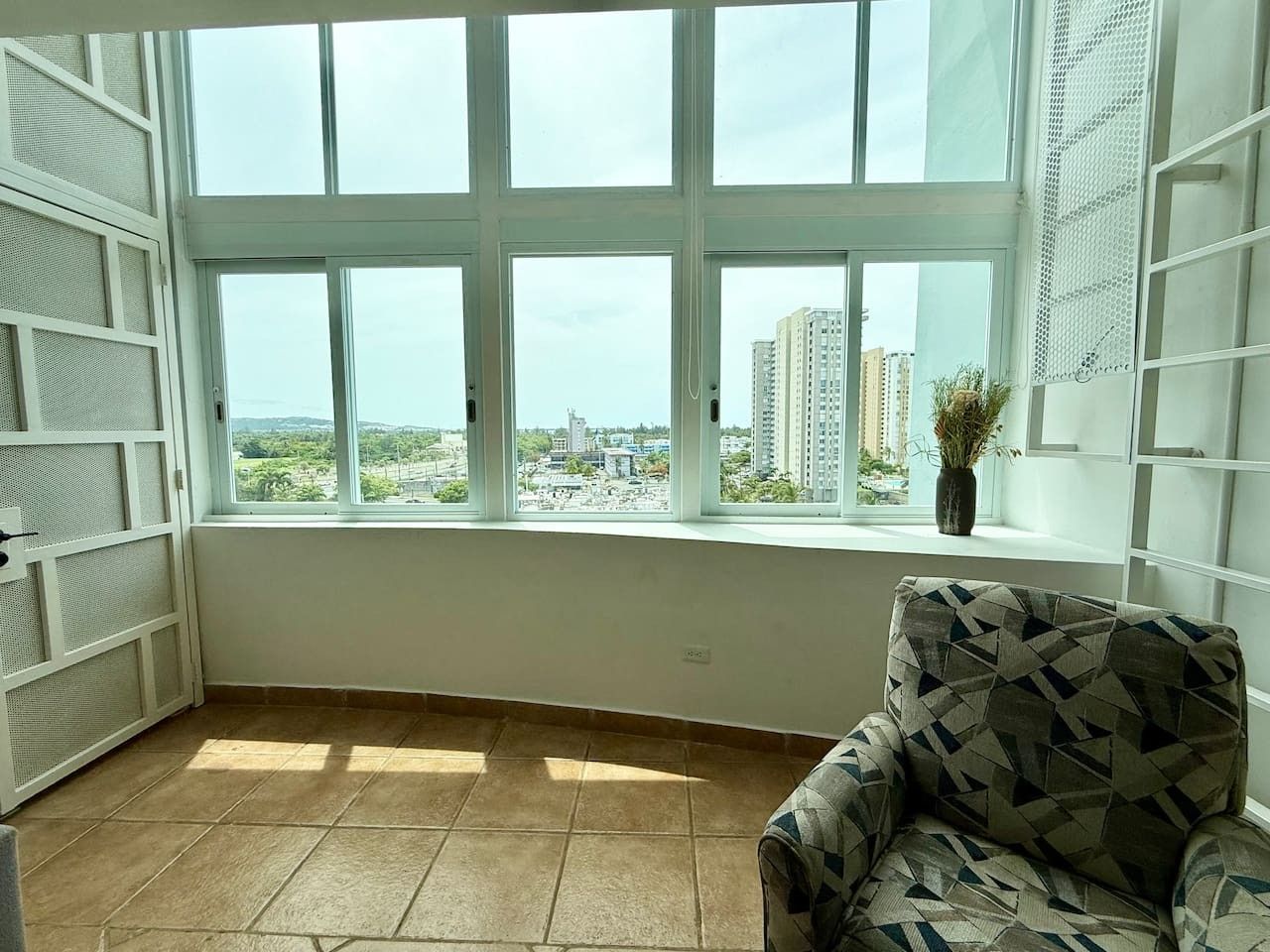 A room with a large window, a patterned armchair, and a potted plant.