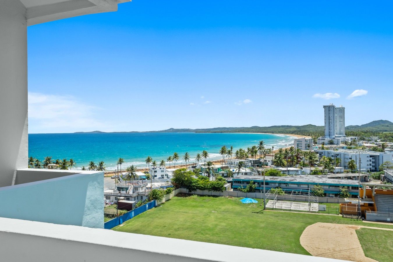 A view from a balcony overlooking a beach with buildings and palm trees.