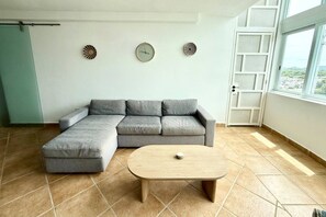 Un salon avec un canapé d’angle, une table basse ronde et une grande fenêtre.