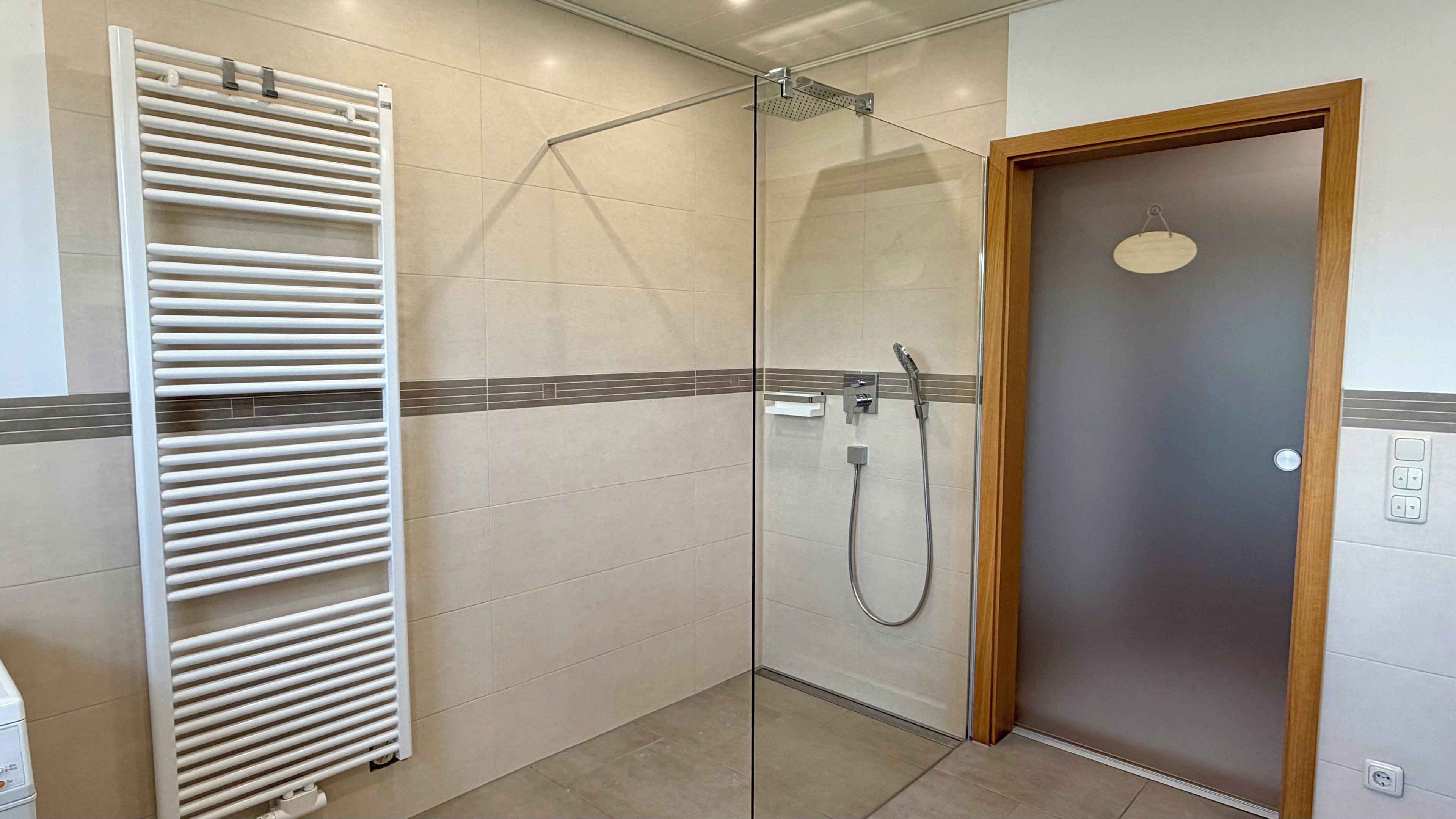 Une salle de bain avec une douche à parois de verre, un porte-serviettes blanc et une porte en bois.