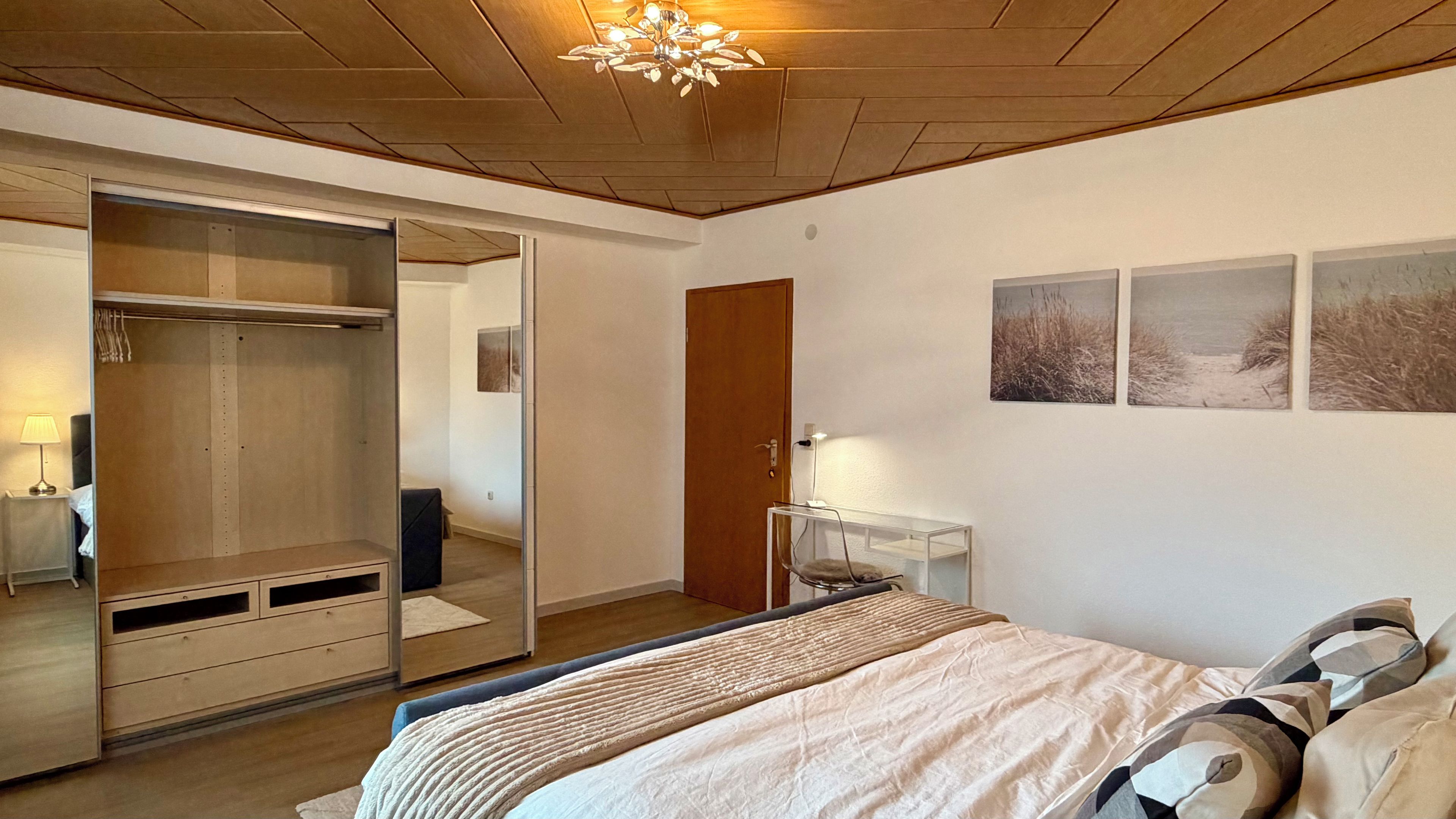 Ein Schlafzimmer mit Bett, Kleiderschrank, Schreibtisch und einer Tür.