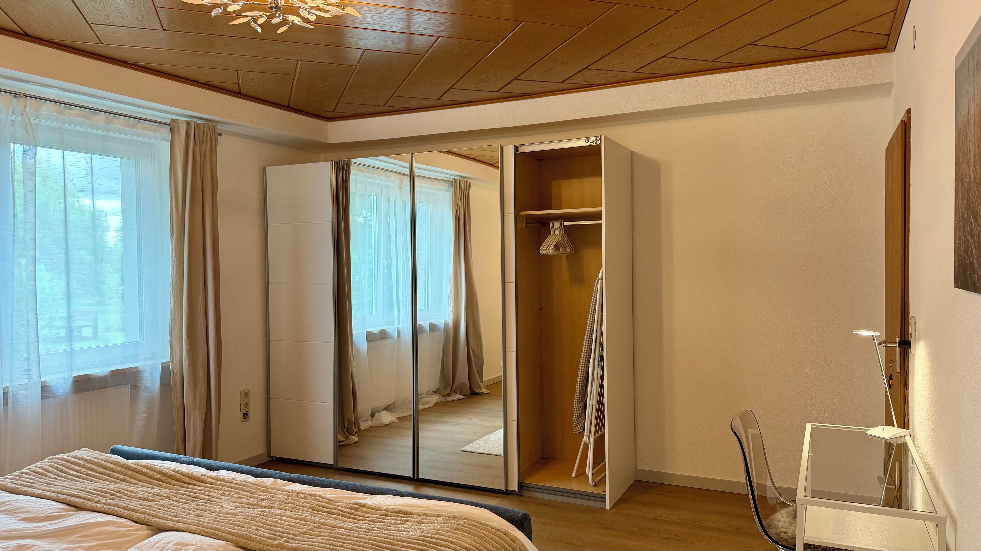 A bedroom with a bed, a wardrobe, a mirror, and a window with curtains.