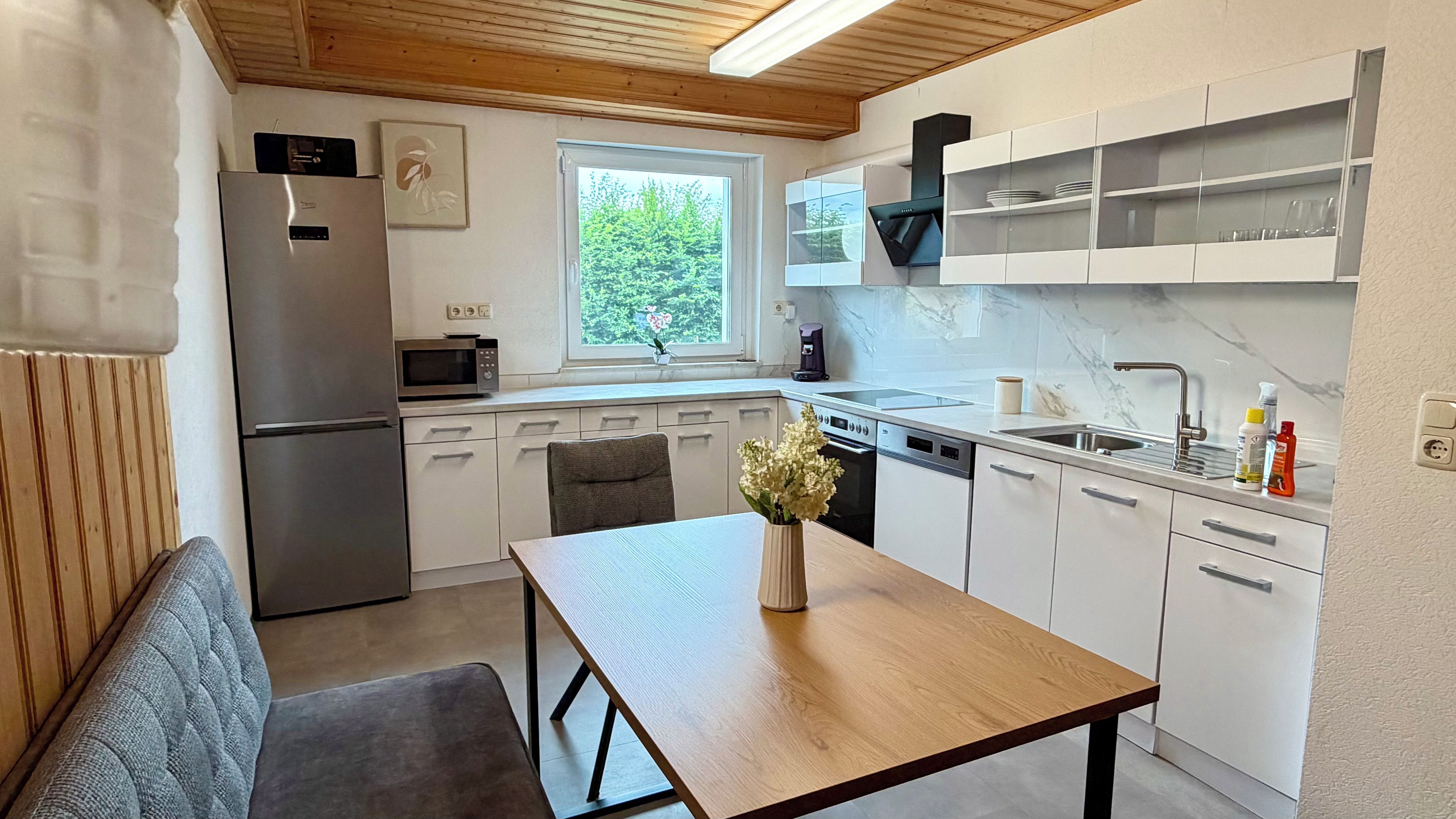 A compact kitchen with a refrigerator, microwave, and dishwasher. There's a window with a view of greenery outside.