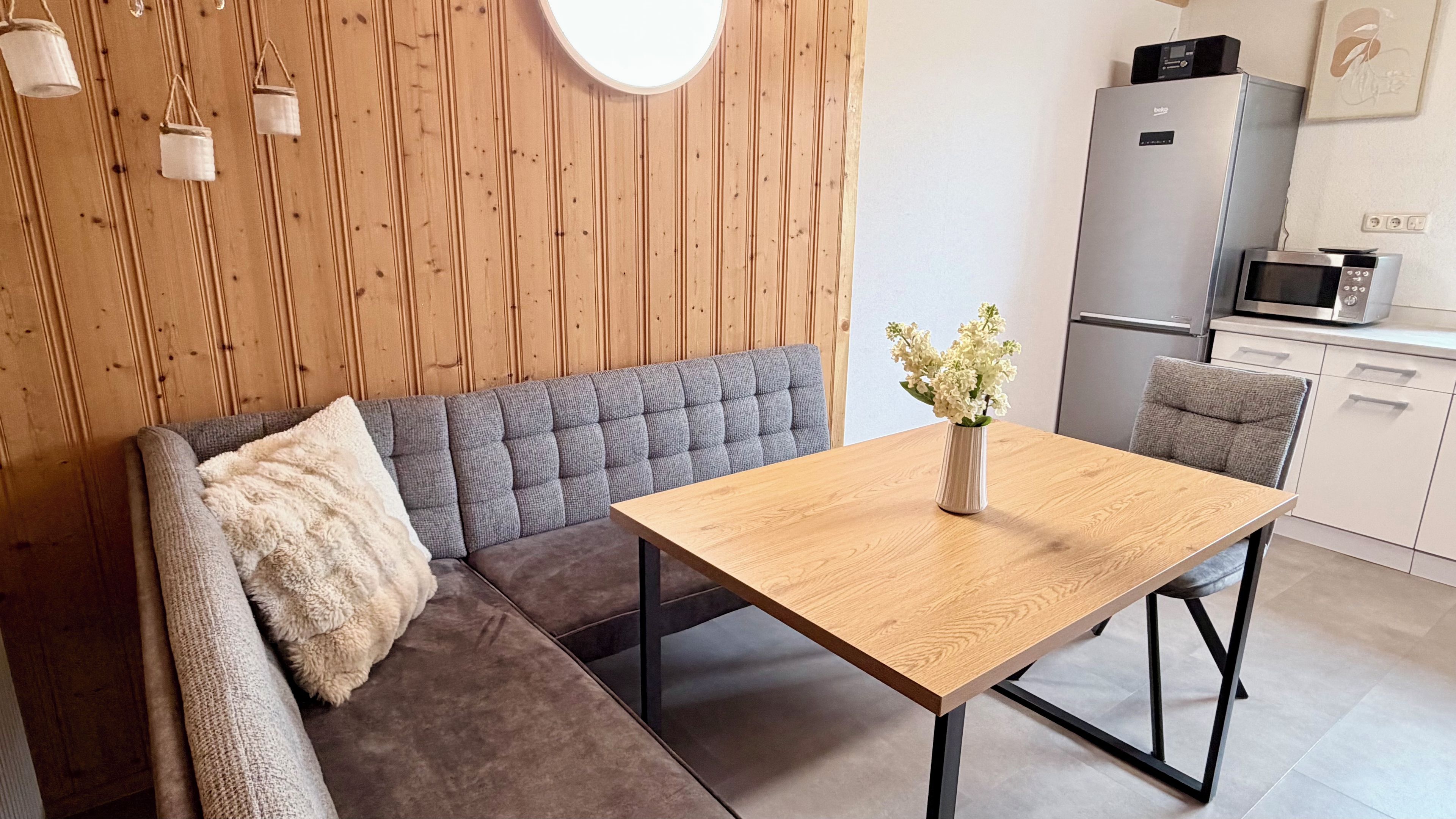 A modern kitchenette with a microwave, refrigerator, and a dining area with a wooden table and sofa.