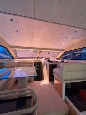 A boat interior with a dining area, seating, and a control panel.