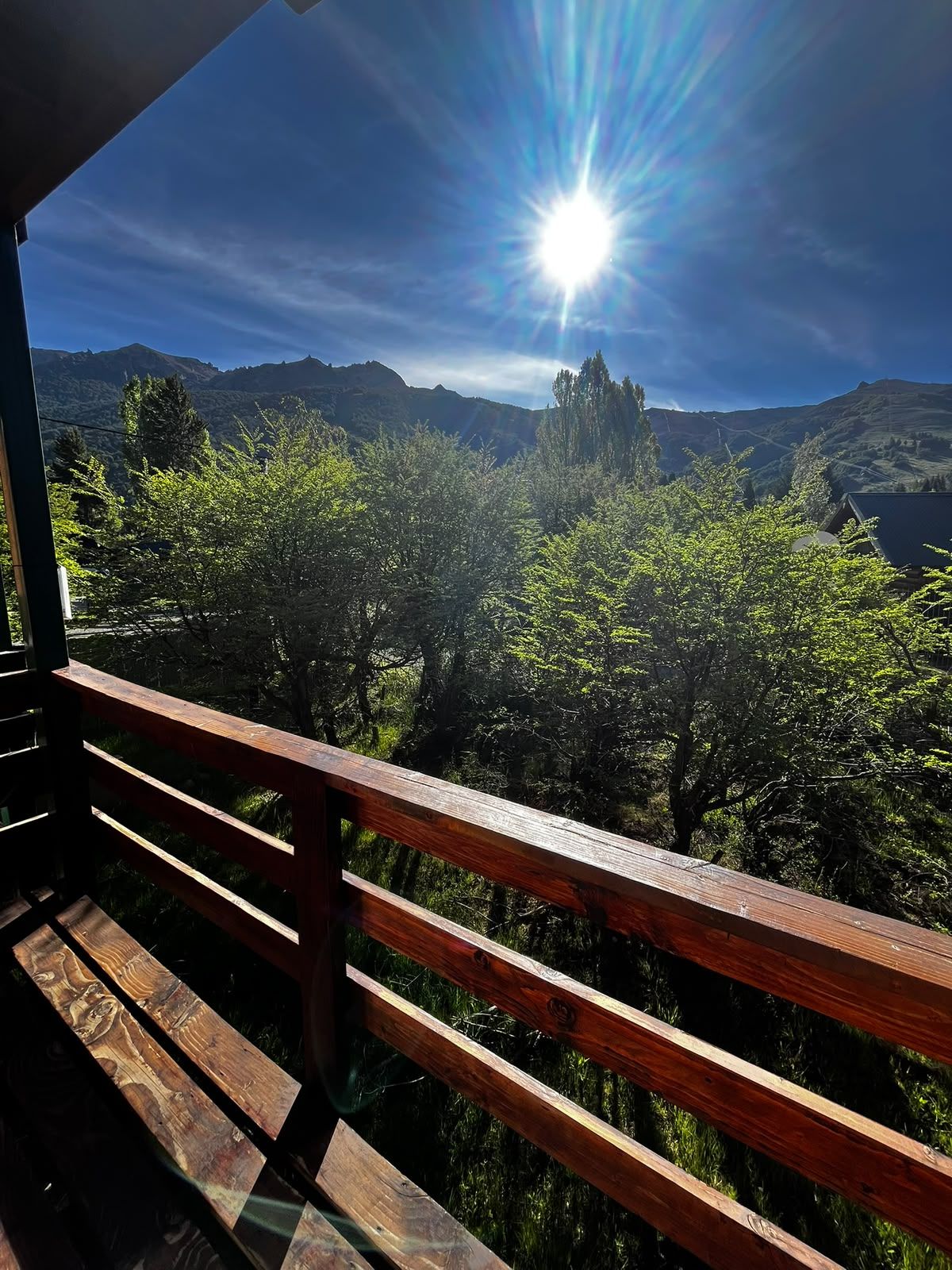 Un balcon en bois offrant une vue sur un paysage montagneux et sur un soleil éclatant.